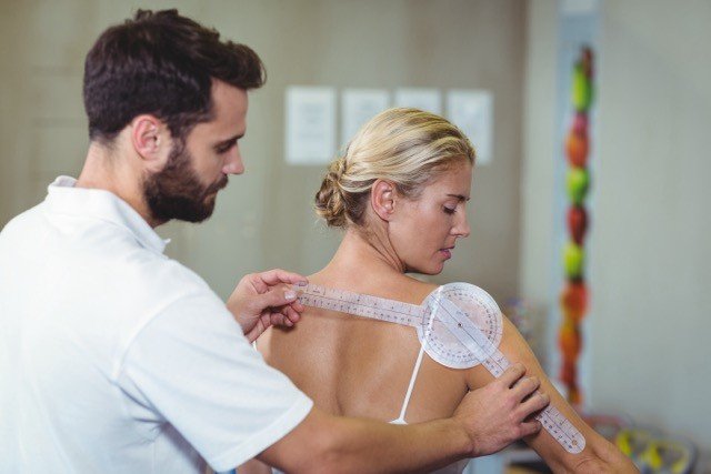 Male therapist measuring female patient back with goniomete in clinic